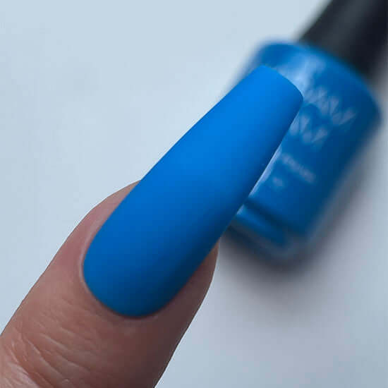 Blue nail polish on a finger with a blurred bottle in the background