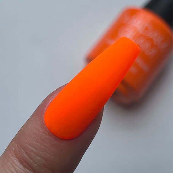 Orange nail polish on a finger with a blurred bottle in the background