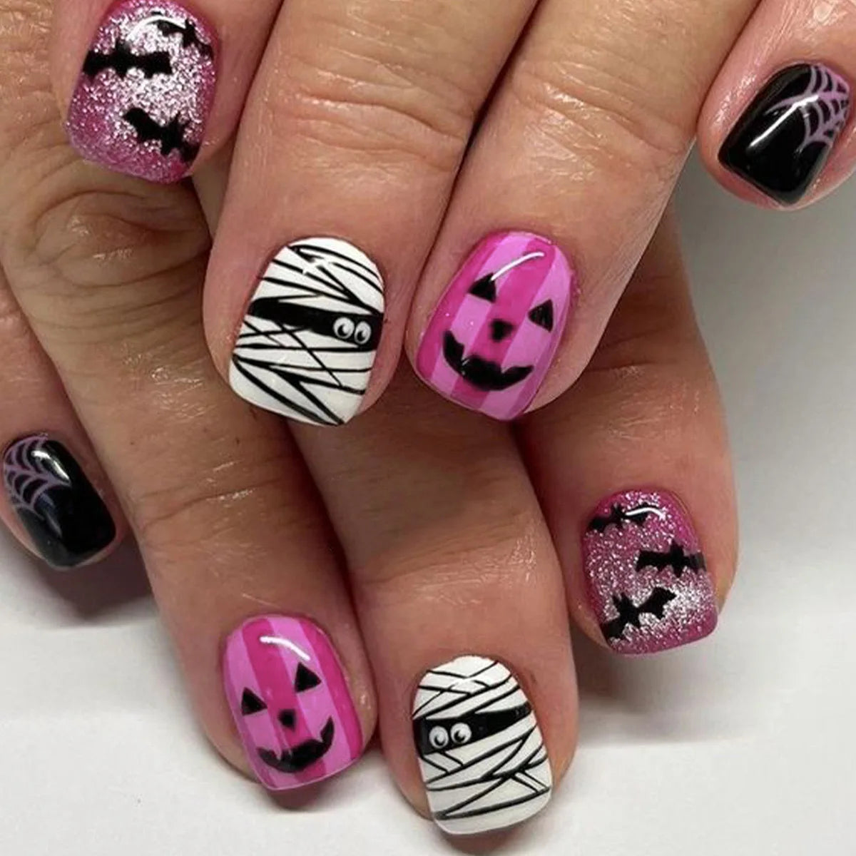 Halloween-themed nail art on a hand with pink, black, and white designs.