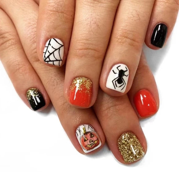 Halloween-themed nail art on a hand with various designs including a spider, pumpkin, and gold glitter.