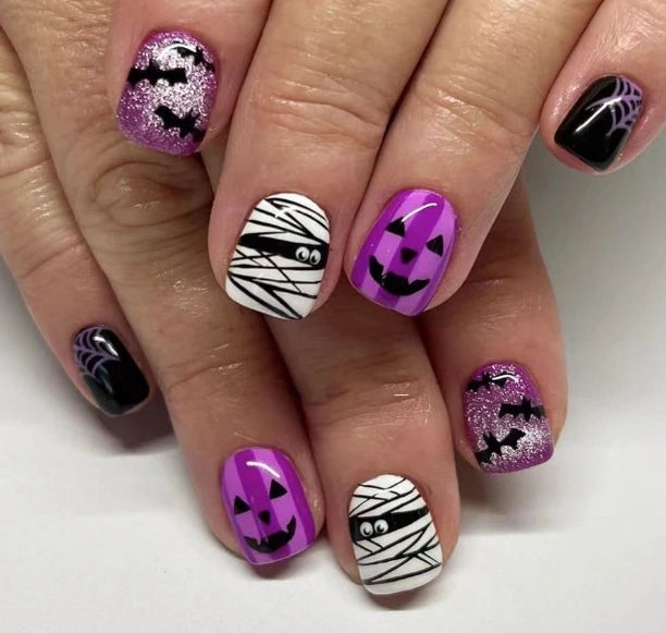 Halloween-themed nail art on a hand with purple, black, and white designs.