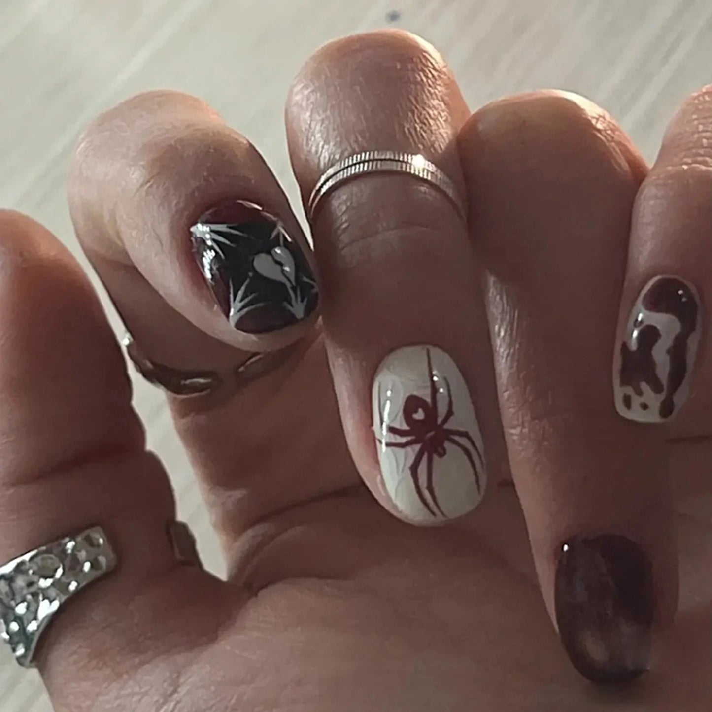 Hand with Halloween-themed nail art featuring spiders and ghosts.