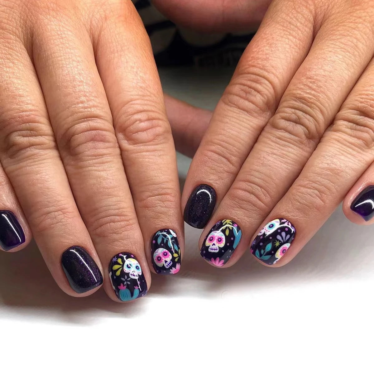 Close-up of hands with dark purple nail polish and colorful skull designs on a white background