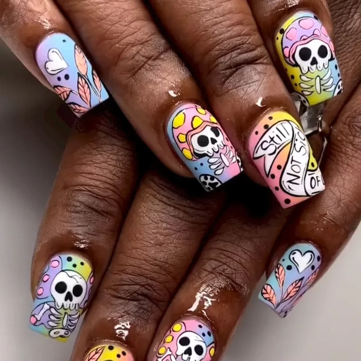 Nails with colorful skull and text designs on a neutral background