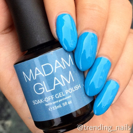 Blue gel polish bottle held by a hand with matching blue nails, branded 'MADAM GLAM'.