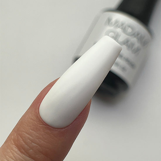 Close-up of a white painted fingernail with a nail polish bottle in the background.
