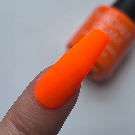 Orange nail polish on a finger with a blurred bottle in the background