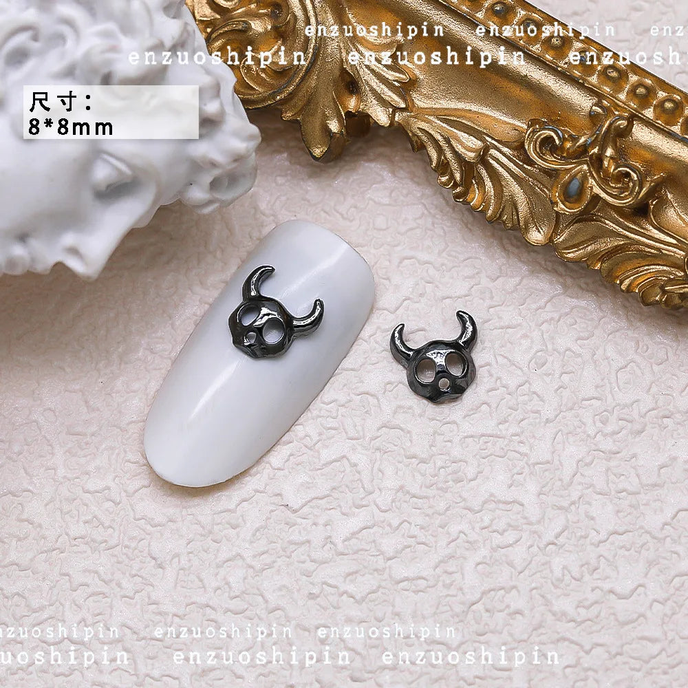 Black nail art decorations on a white nail with gold decorative item in the background