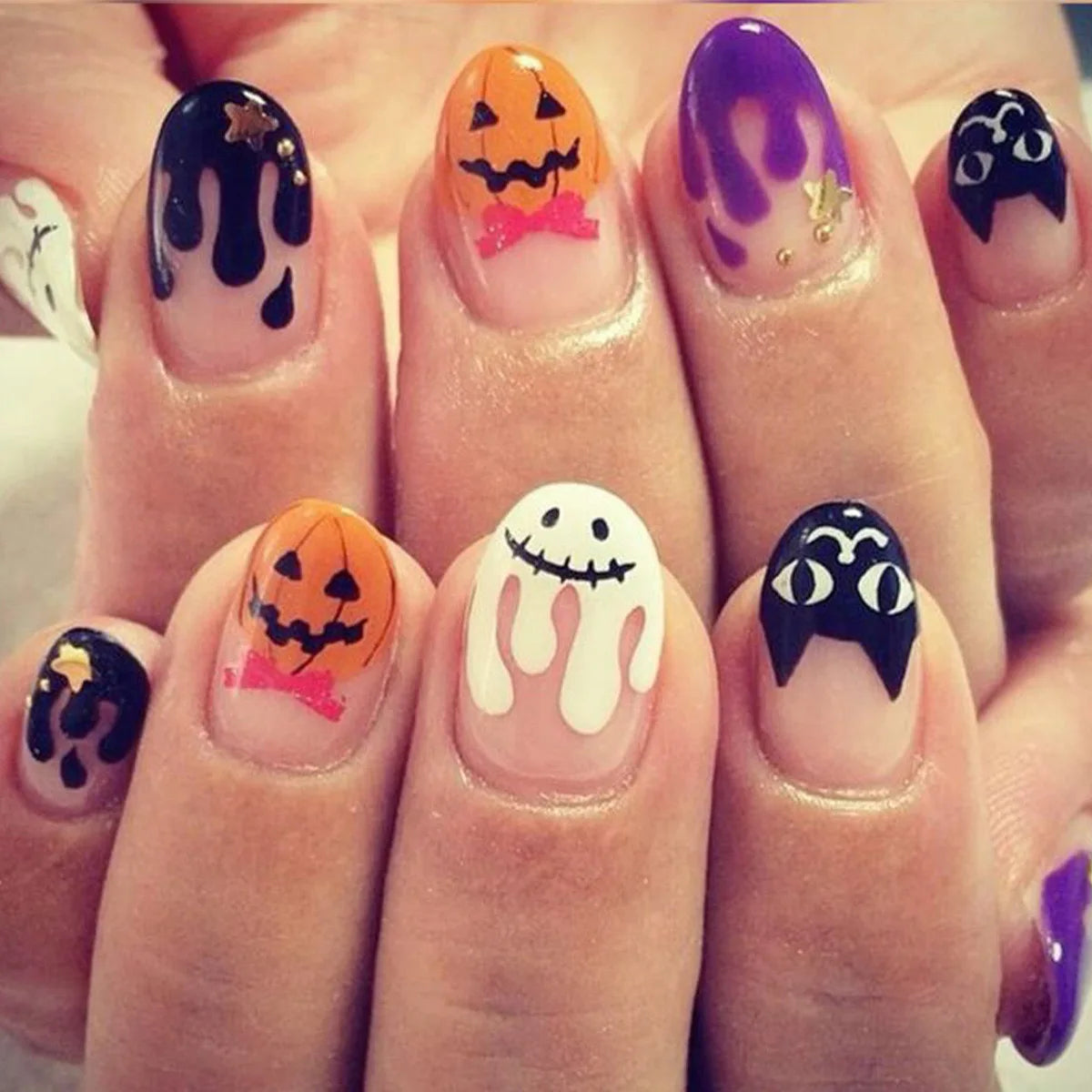 Halloween-themed nail art on a hand with various designs including pumpkins, ghosts, and cats.