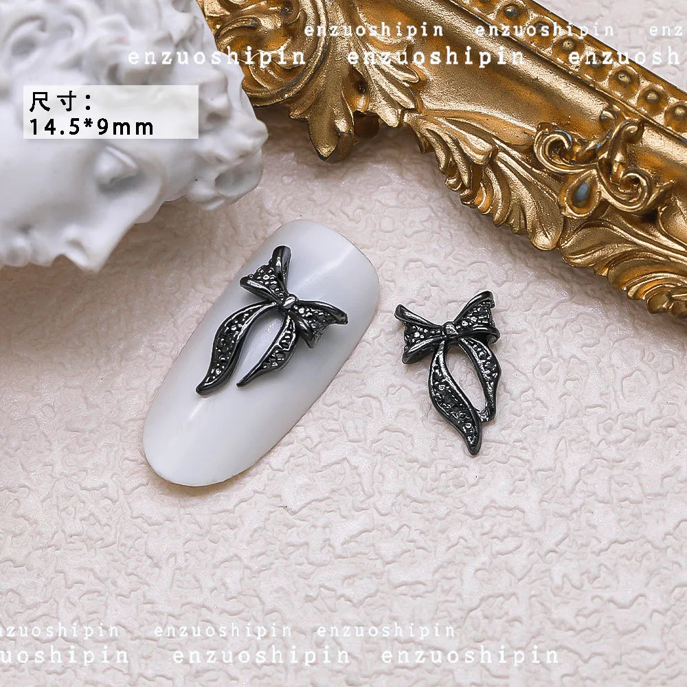 Decorative black bow nail art charm on a white nail with gold decorative background