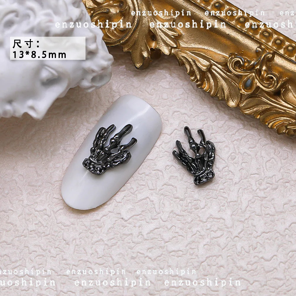 Black hand-shaped nail art decorations on a white nail with gold and white decorative elements in the background.