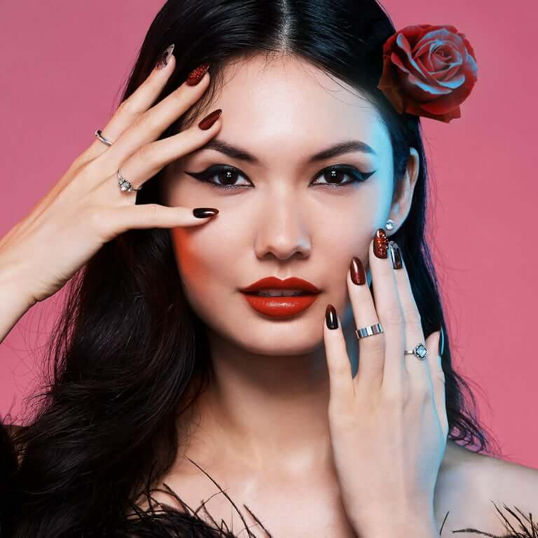 Woman with dark hair, red lipstick, and decorative nails against a pink background